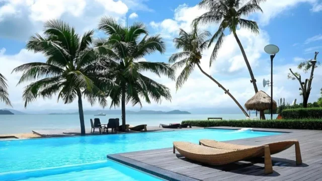 Beachfront pool with sun loungers under palms at The Blue Sky Resort Koh Payam